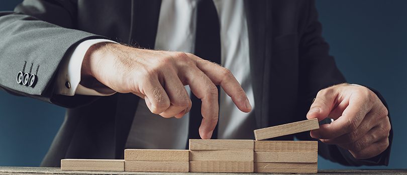 Business vision and progress Businessman assembling stairway of wooden pegs as he walks his fingers upwards in a conceptual image.