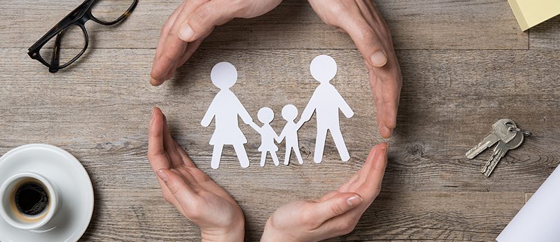 Family care Close up of female and male hands protecting a paper chain family. Top view of two hands form a circle around white paper chain family on wooden table. Family care, insurance and helping hand concept.