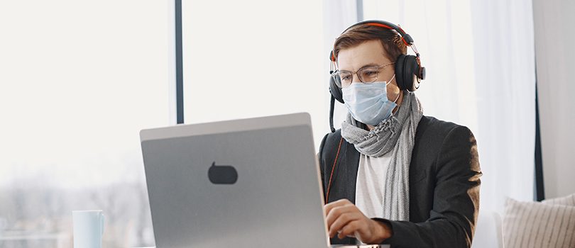 Male has lesson online e-learning in internet concept Male in a medical mask. Man sitting in living room at home. Guy enjoying studying on quarantine.
