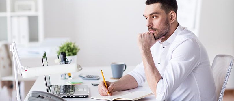 businessman with laptop and notebook at office business and people concept - businessman with laptop and notebook sitting at office table and thinking