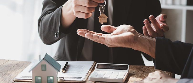 A home rental company employee is handing the house keys to a customer who has agreed to sign a rental contract, explaining the details and terms of the rental. Home and real estate rental ideas.