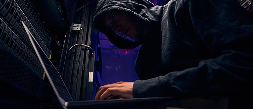Expert cybercriminal installing malware using his laptop Low angle of hacker carrying out cyberattack on data center computer system in server room