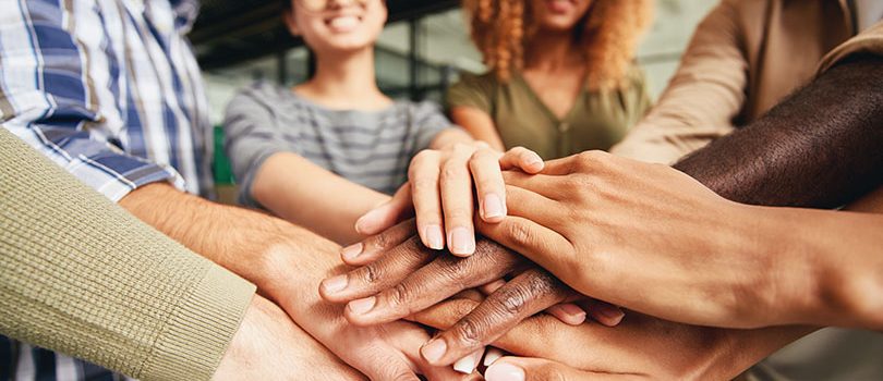 Selective focus photo of hands with different skin tone being put together by cheerful young people from various countries