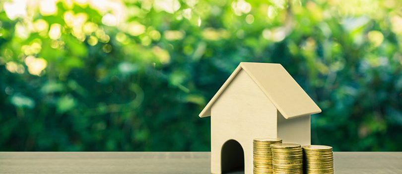Property investment, Home loan, reverse mortgage concept. A smal Property investment, Home loan, reverse mortgage concept. A small house model with stack of gold coins on wooden table with nature background and empty space at left hand for your text.
