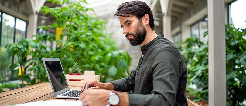 Young man with laptop sitting indoors in green office, working. Portrait of young man with laptop sitting indoors in green office, working.