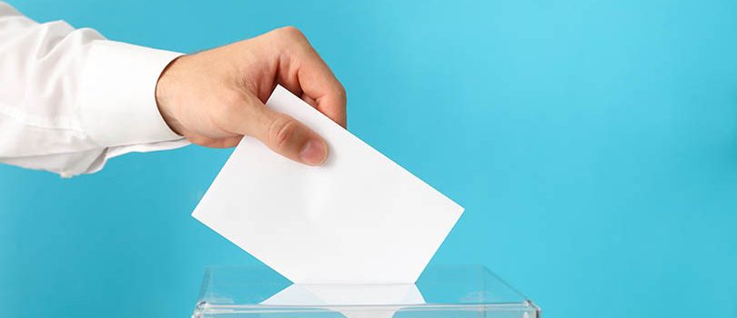 Man putting ballot into voting box on blue background Man putting ballot into voting box on blue background