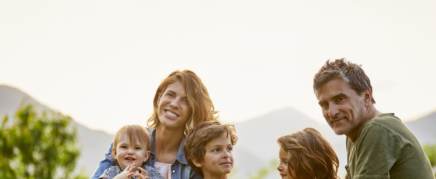 Portrait of happy parents with children. Family is sitting on retaining wall against sky. They are in casuals.